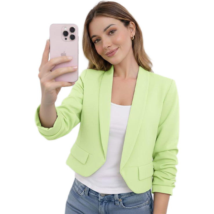 Woman wearing a light green blazer over a white top and blue jeans, holding a pink phone.