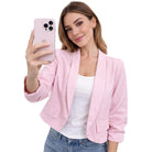 Woman wearing a pink blazer over a white top and blue jeans, holding a pink phone.