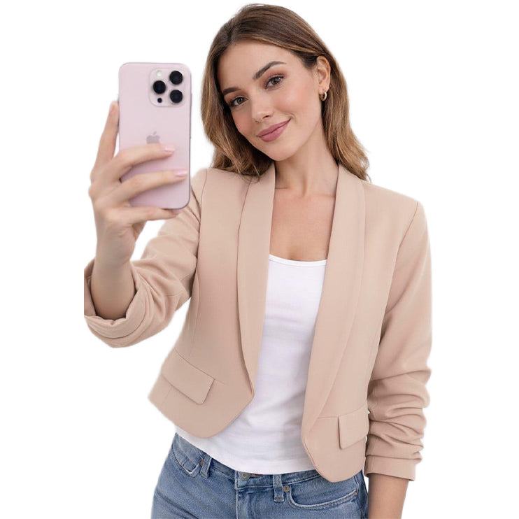 Woman taking a selfie with a pink phone, wearing a beige blazer over a white top and blue jeans on a white background