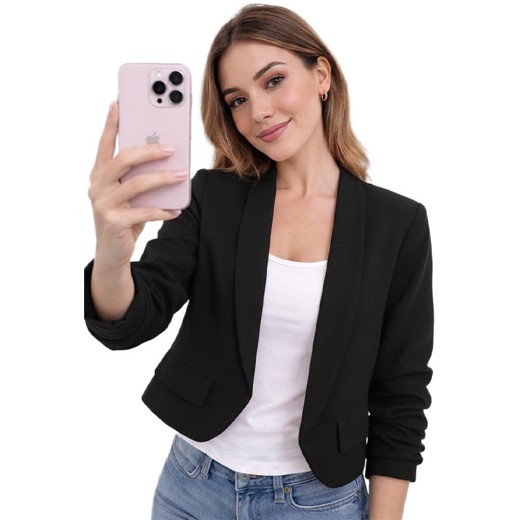 Woman taking a selfie with a pink phone, wearing a black blazer over a white top and blue jeans on a white background