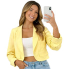 Woman wearing a yellow blazer taking a selfie on a white background