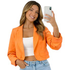 Woman wearing an orange blazer and taking a selfie on a white background