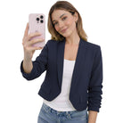 Woman taking a selfie wearing a navy blazer and white top on a white background